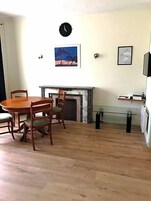 Quarto com mesa de jantar de madeira, cadeiras, lareira, relógio e quadros na parede.