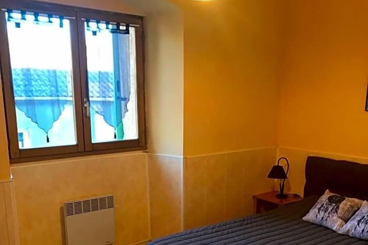 Una habitación con una cama, una ventana, un calentador y una mesita de noche con lámpara.