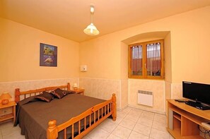 Quarto com cama, televisão, janela e um quadro na parede.