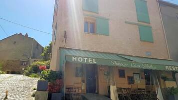 Un hôtel avec un auvent vert, des tables à l’extérieur et une rue pavée.