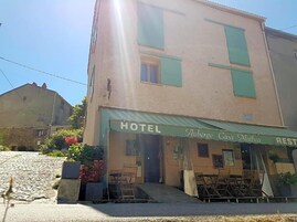 Um hotel com toldo verde, mesas ao ar livre e rua de calçada.
