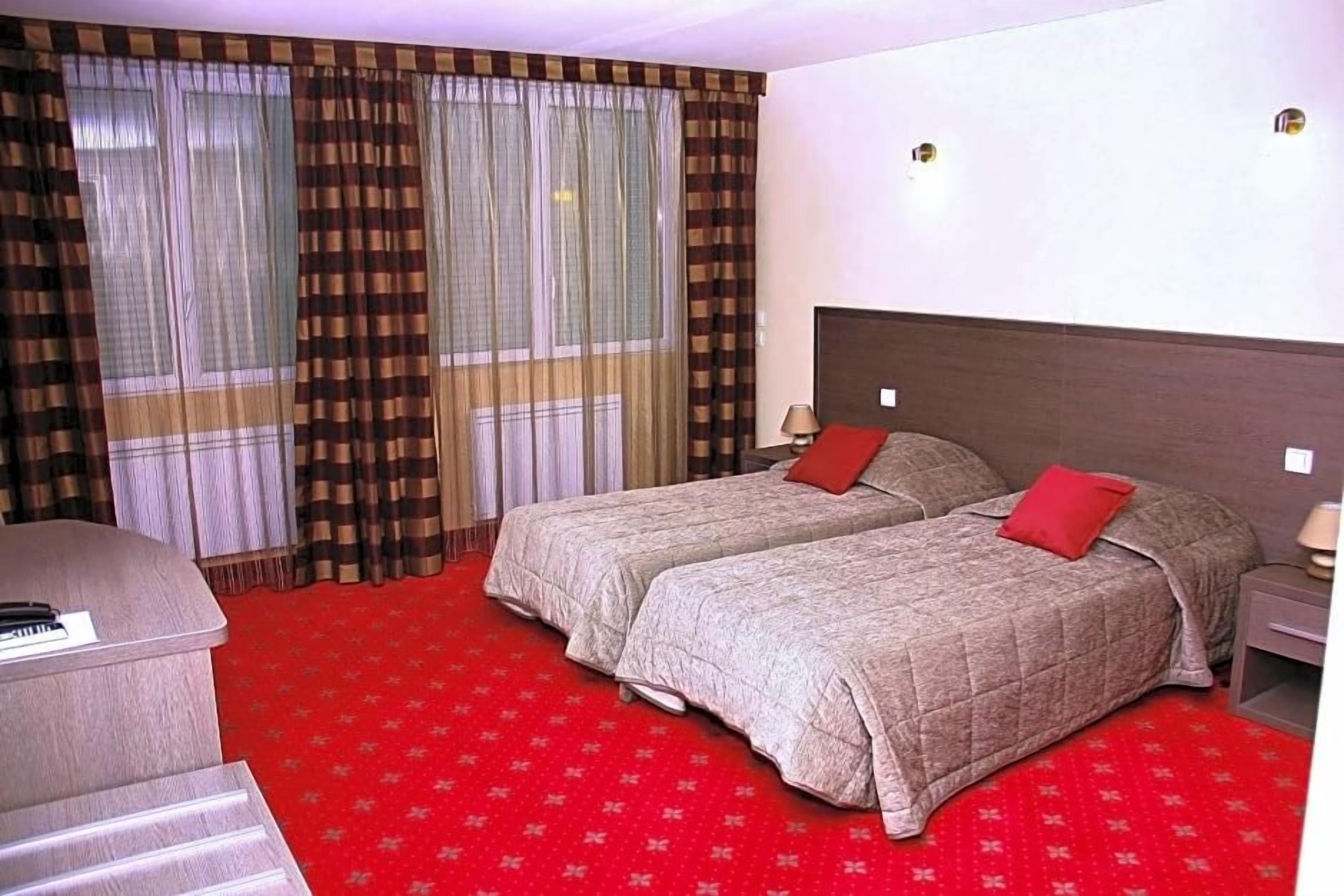 Een hotelkamer met twee bedden, een bureau en een rood tapijt.