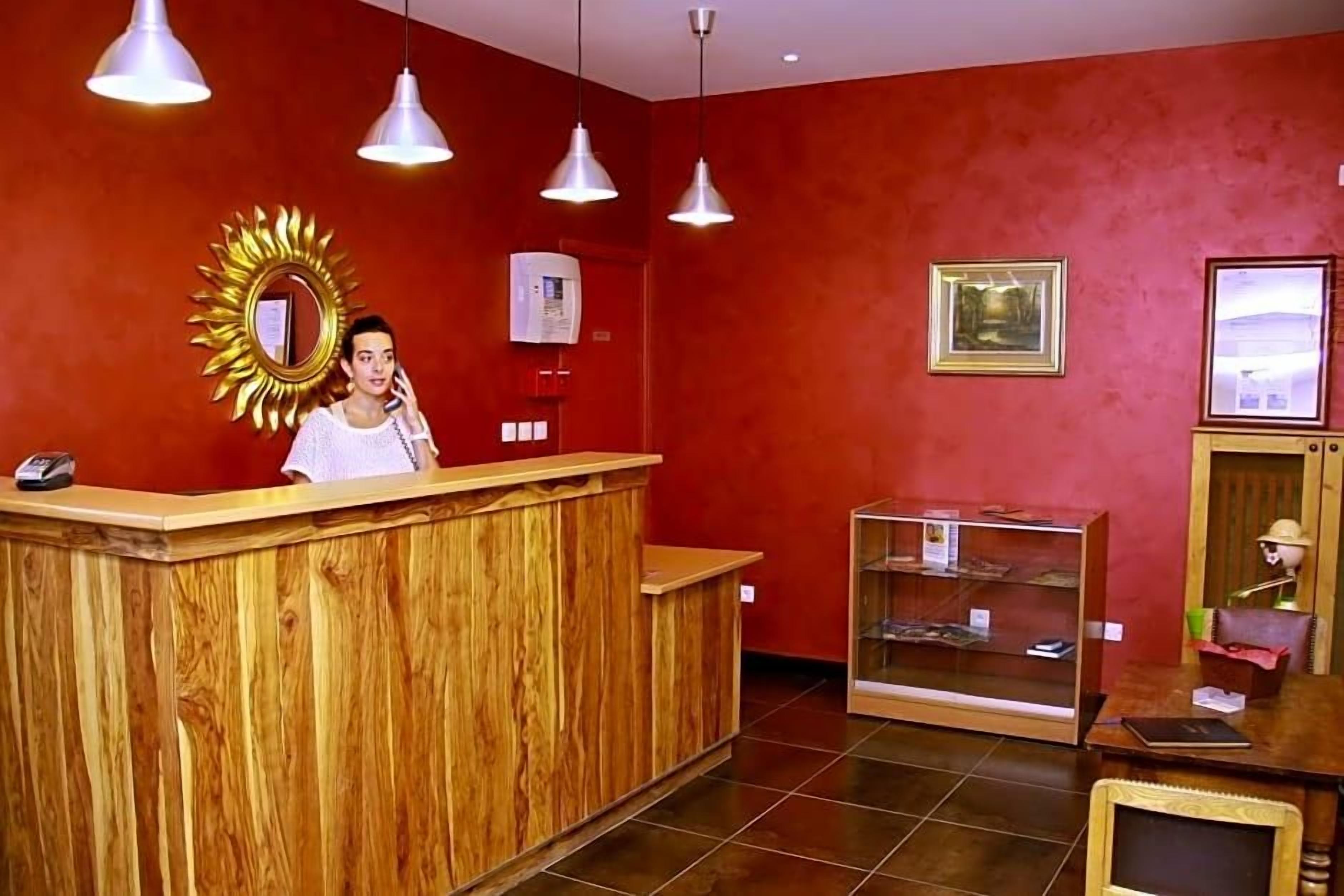 Een receptiegedeelte met een houten balie, hangende verlichting, een zonneschijfspiegel en een glazen vitrine.