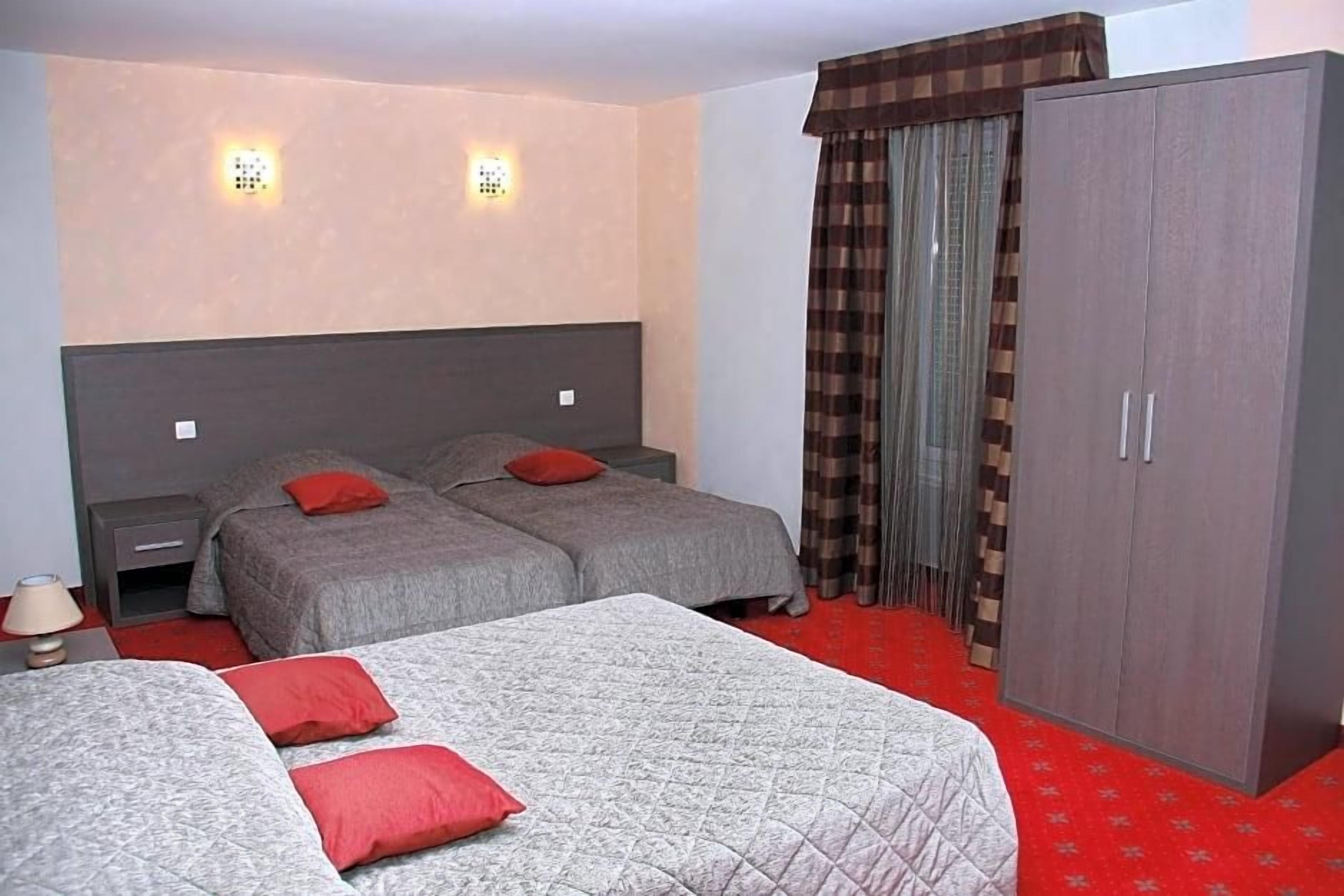 A hotel room with two beds, a wardrobe, and a red carpet.