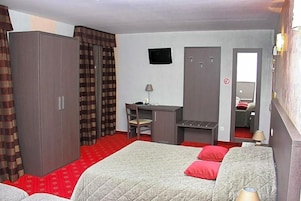 Quarto de hotel com cama, escrivaninha, armário e televisão.