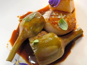 A dish with scallops and a green vegetable, possibly artichoke, on a white plate with sauce.