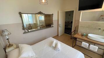 Una camera d'albergo con un letto, un grande specchio, una televisione, un comodino e un bagno con lavandino e specchio.