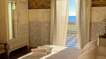 Una camera da letto con un letto, un armadio e vista sul mare attraverso tende leggere.