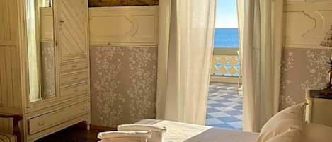 A bedroom with a bed, a wardrobe, and a view of the sea through sheer curtains.