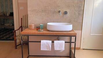 Un bagno con un lavandino bianco su un mobiletto in legno, un porta asciugamani con due asciugamani e uno specchio sopra il lavandino.