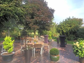An outdoor patio area with multiple tables and chairs, surrounded by potted plants and trees. - Hotel Wuelfers Gasthaus (Groß Ippener)