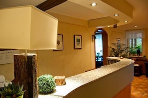 A reception area with a counter, framed pictures on the wall, a wooden post, and a small plant. - Hotel & Restaurant Ernst (Giesen)