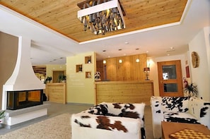 A hotel lobby with a fireplace, wooden reception desk, and a sofa with a cowhide pattern. - Hotel Chalet Dlaces (Selva di Val Gardena)
