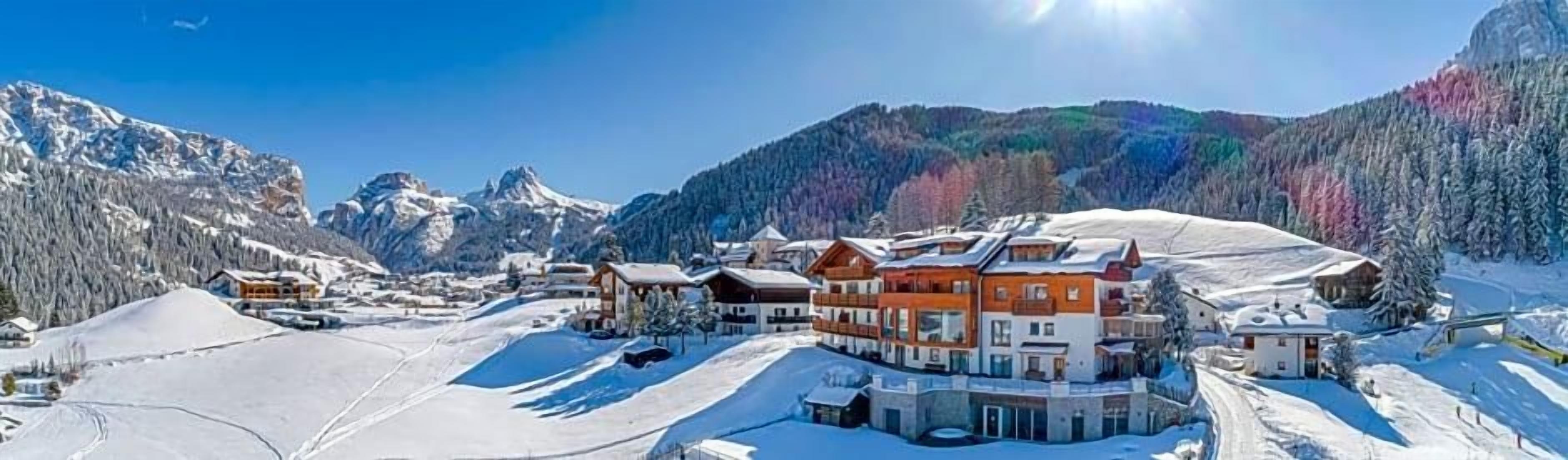 Un complejo turístico invernal cubierto de nieve, con varios edificios, incluyendo una estructura destacada con techo rojo, rodeado de laderas nevadas y árboles.
