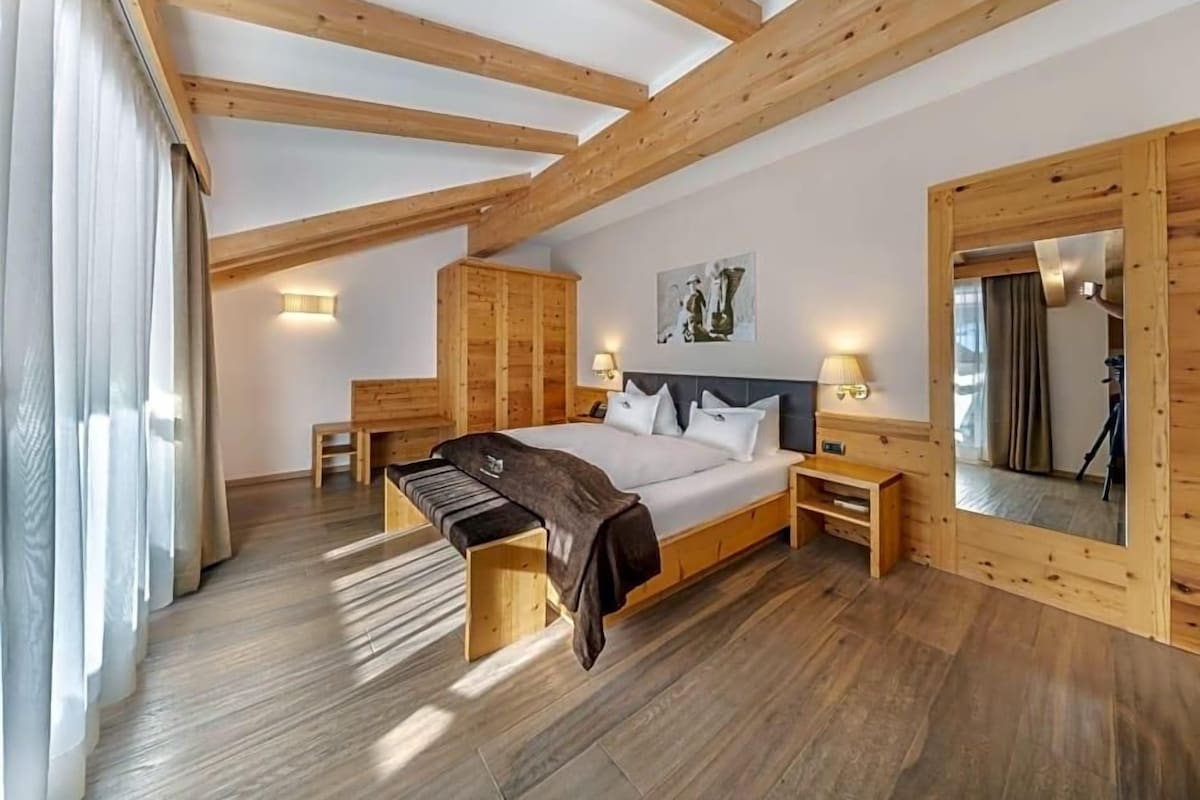 A bedroom with a wooden ceiling, a bed, bedside tables, a wardrobe, and a mirror.