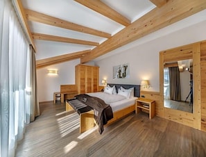 A bedroom with a wooden ceiling, a bed, bedside tables, a wardrobe, and a mirror. - Hotel Chalet Dlaces (Selva di Val Gardena)