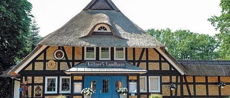 Un edificio tradicional con entramado de madera y techo de paja, una puerta azul y un letrero que dice 'Köllner's Landhaus'.