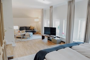 Een hotelkamer met een bed, een televisie, een bank, een bijzettafeltje en een raam met gordijnen.