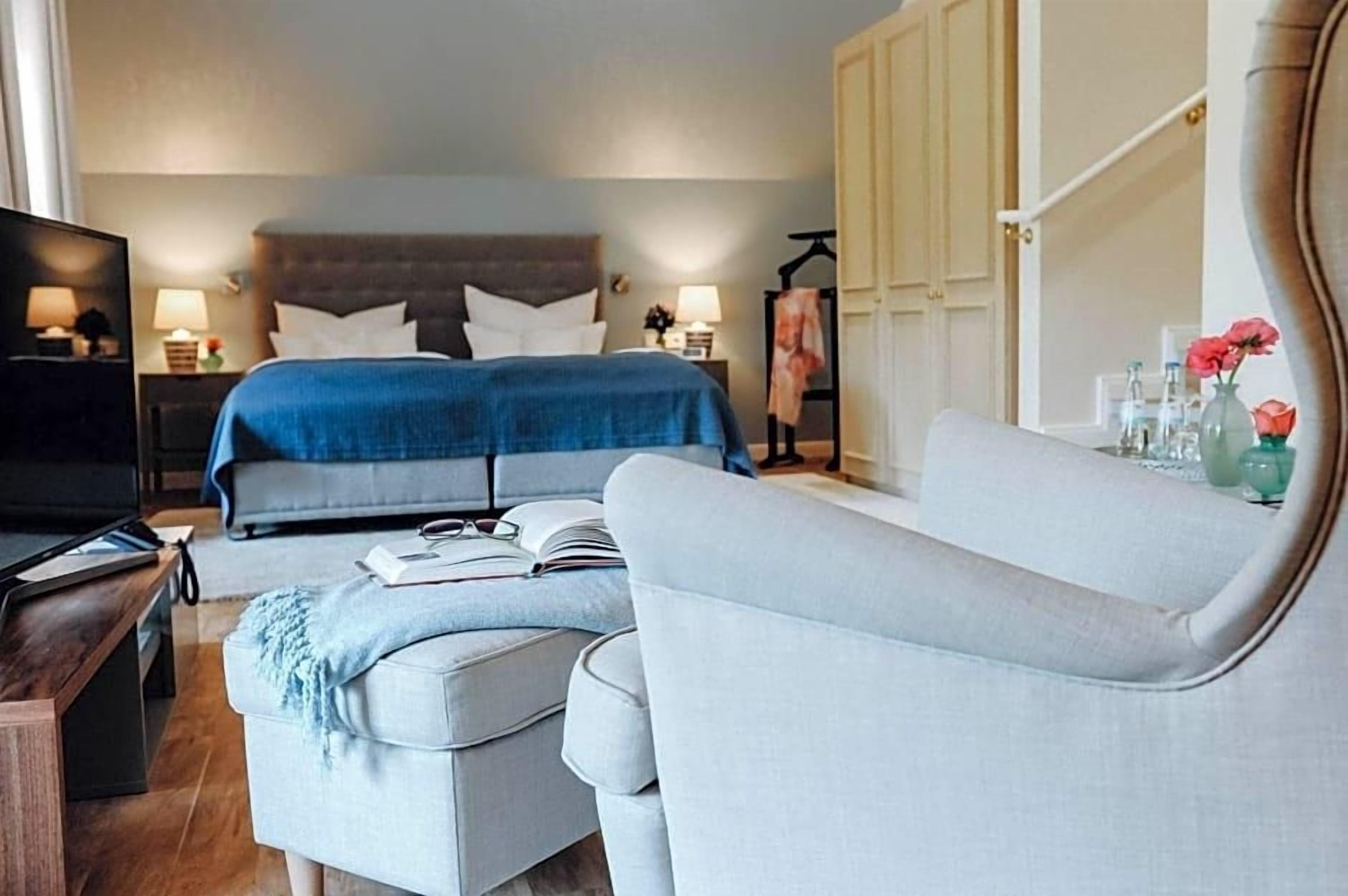 A hotel room with a bed, a sofa, a TV, and a desk with a lamp.