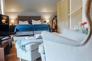 A hotel room with a bed, a sofa, a TV, and a desk with a lamp.