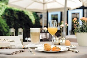 Desayuno con un croissant, un vaso de jugo de naranja, un periódico y un vaso de una bebida blanca, probablemente leche, sobre una mesa con un menú.
