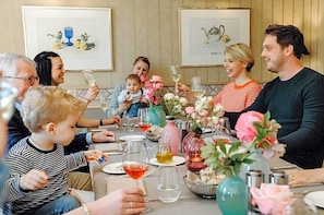 Un grupo de personas sentadas alrededor de una mesa con varios objetos, incluyendo vasos, una jarra y flores.