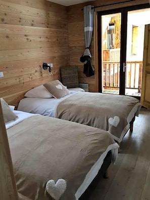 Una habitación de madera con dos camas, una silla y una puerta corredera que da a un espacio exterior.