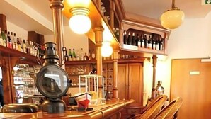 A bar area with wooden bar stools, a large bar lamp, and shelves stocked with bottles. - Hotel Am Dom (Greifswald)