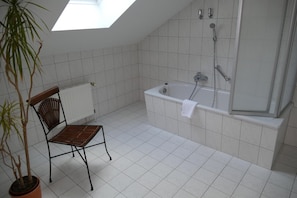 A bathroom with a skylight, a bathtub, a shower, a radiator, and a chair.