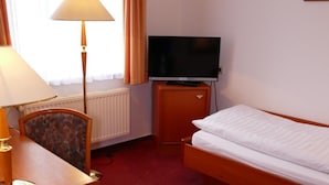 A hotel room with a bed, a desk with a lamp, a television on a stand, and a radiator. - Hotel Am Dom (Greifswald)