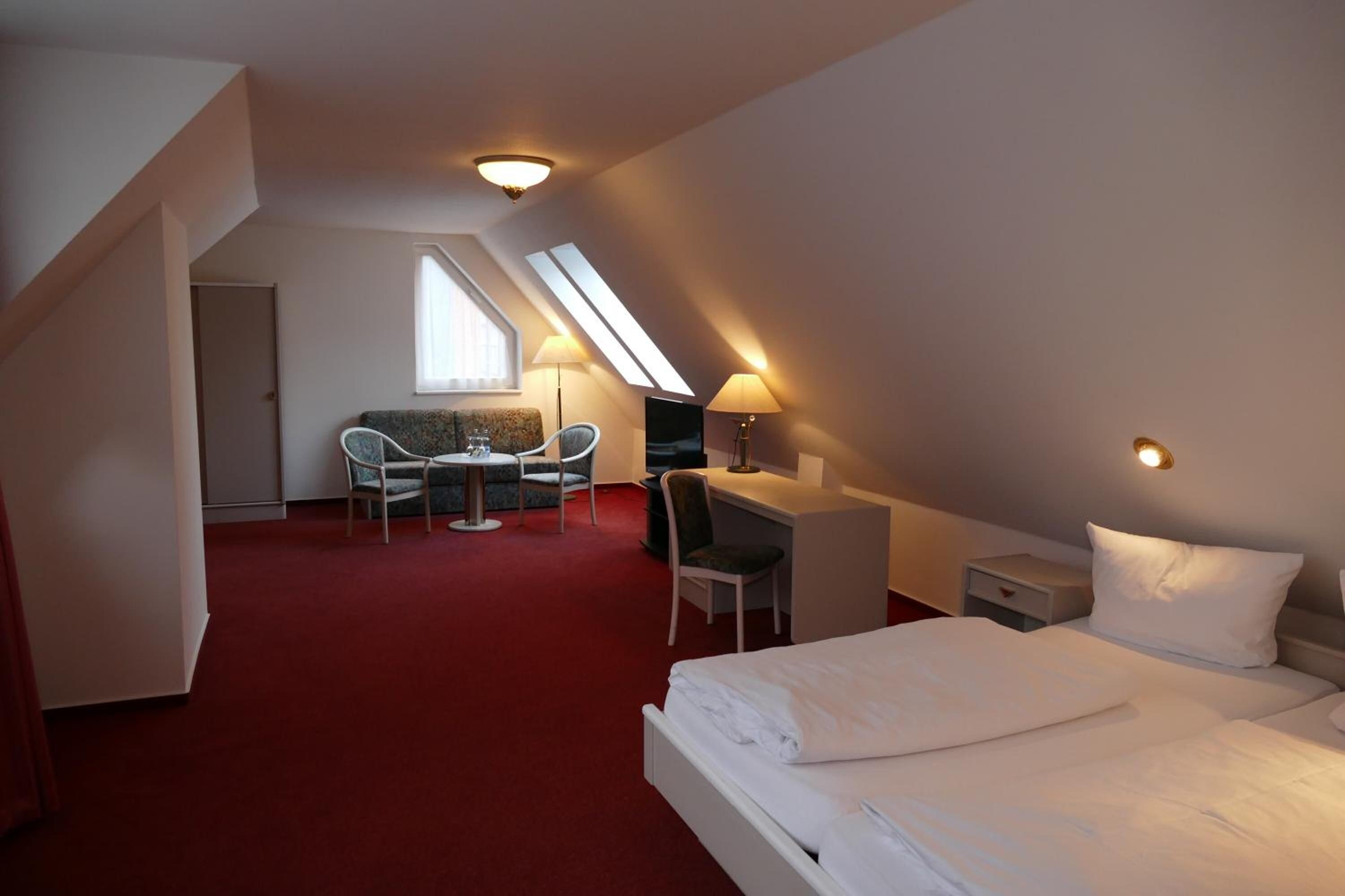 Ett hotellrum med en säng, ett skrivbord, två stolar, ett litet bord och ett fönster.