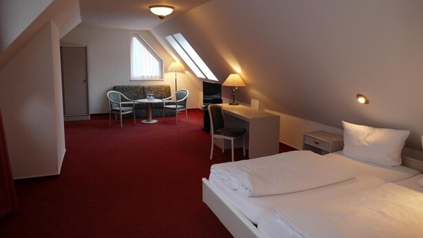 A hotel room with a bed, desk, two chairs, a small table, and a window. - Hotel Am Dom (Greifswald)