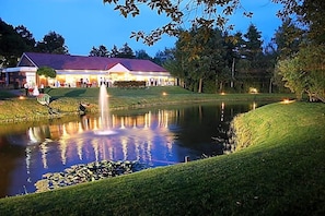 A building with a pond and fountain, surrounded by trees and well-maintained grass. - Hotel Driland (Gronau (Westphalia))