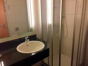 A bathroom with a white sink, a mirror, and a glass-enclosed shower area. - Hotel Driland (Gronau (Westphalia))