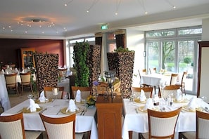 A restaurant with tables set for dining, featuring a central decorative piece and a view of the outdoors. - Hotel Driland (Gronau (Westphalia))