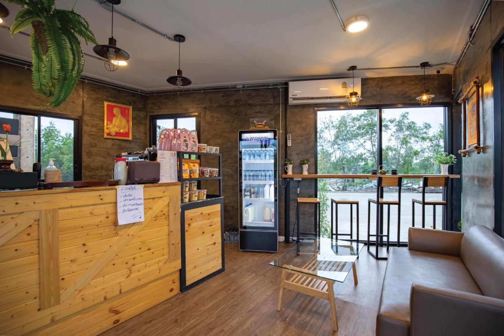Interior de una cafetería con muebles de madera, una barra, un refrigerador y ventanas amplias.