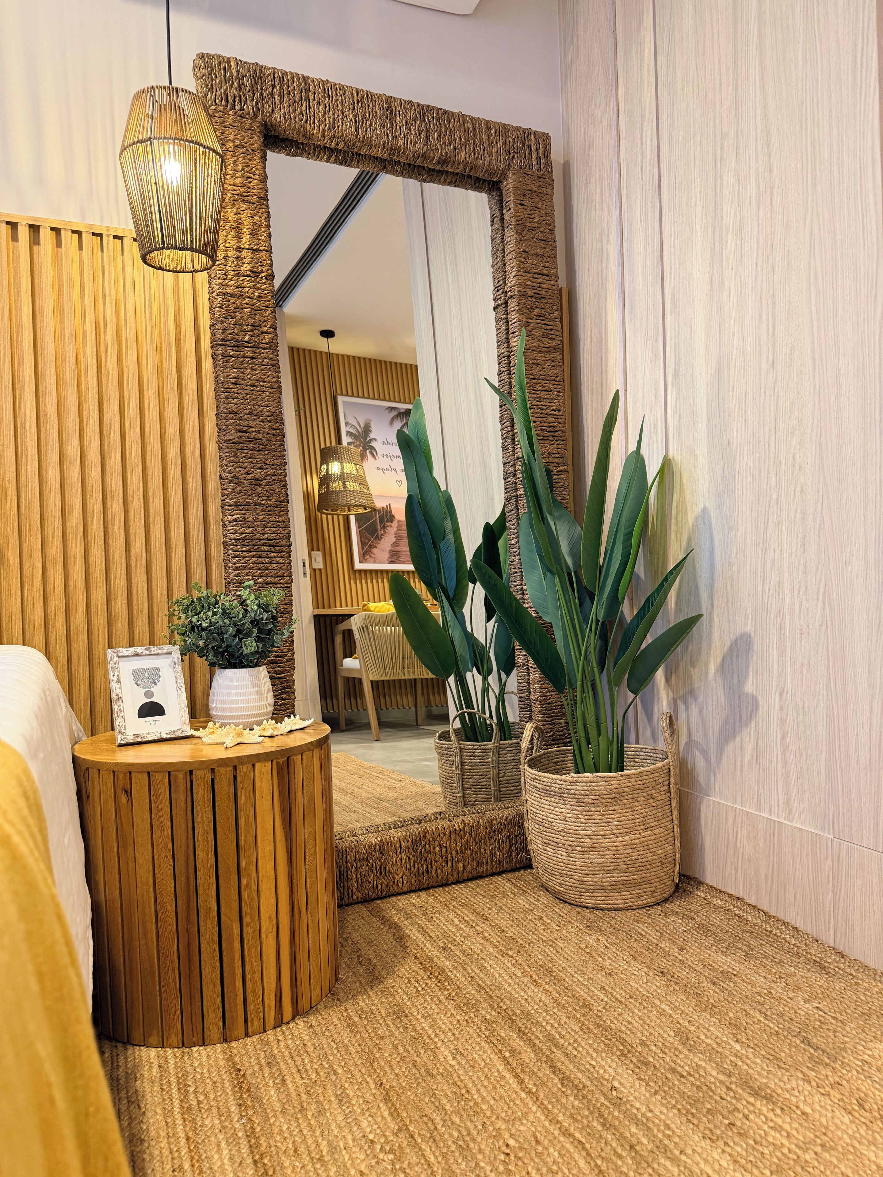 A room with a large mirror, a round wooden table with a plant, and a woven rug.