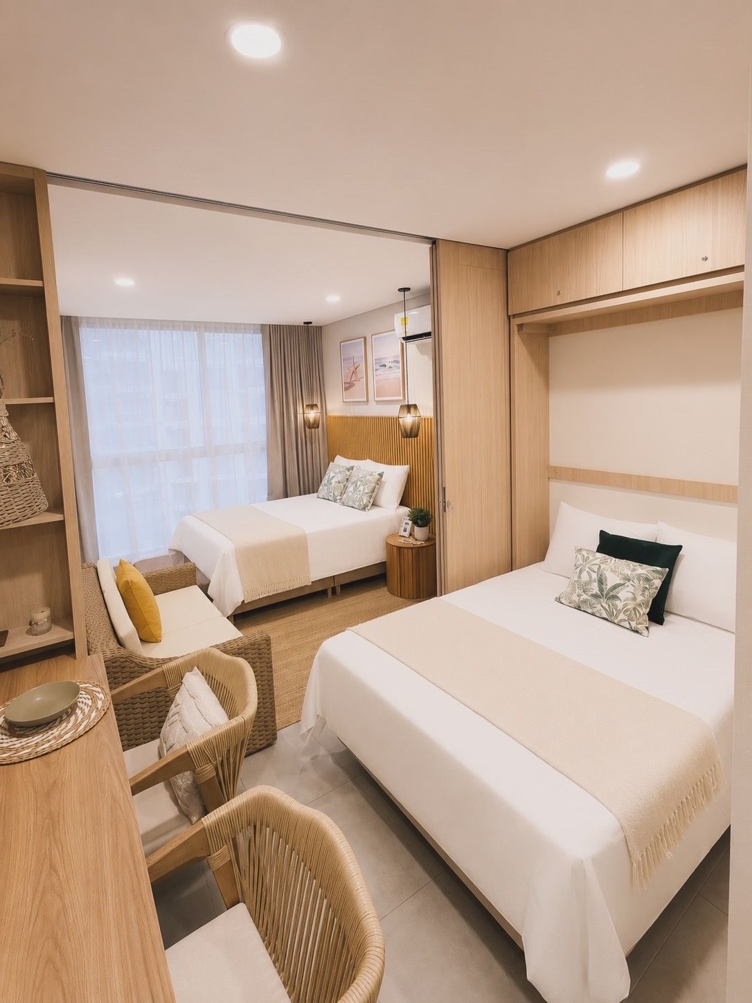 A hotel room with two beds, a sitting area with a chair, a small table, and a bedside table with a lamp.