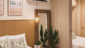 A modern hotel room with a bed, bedside table, potted plants, a mirror, and an air conditioning unit.