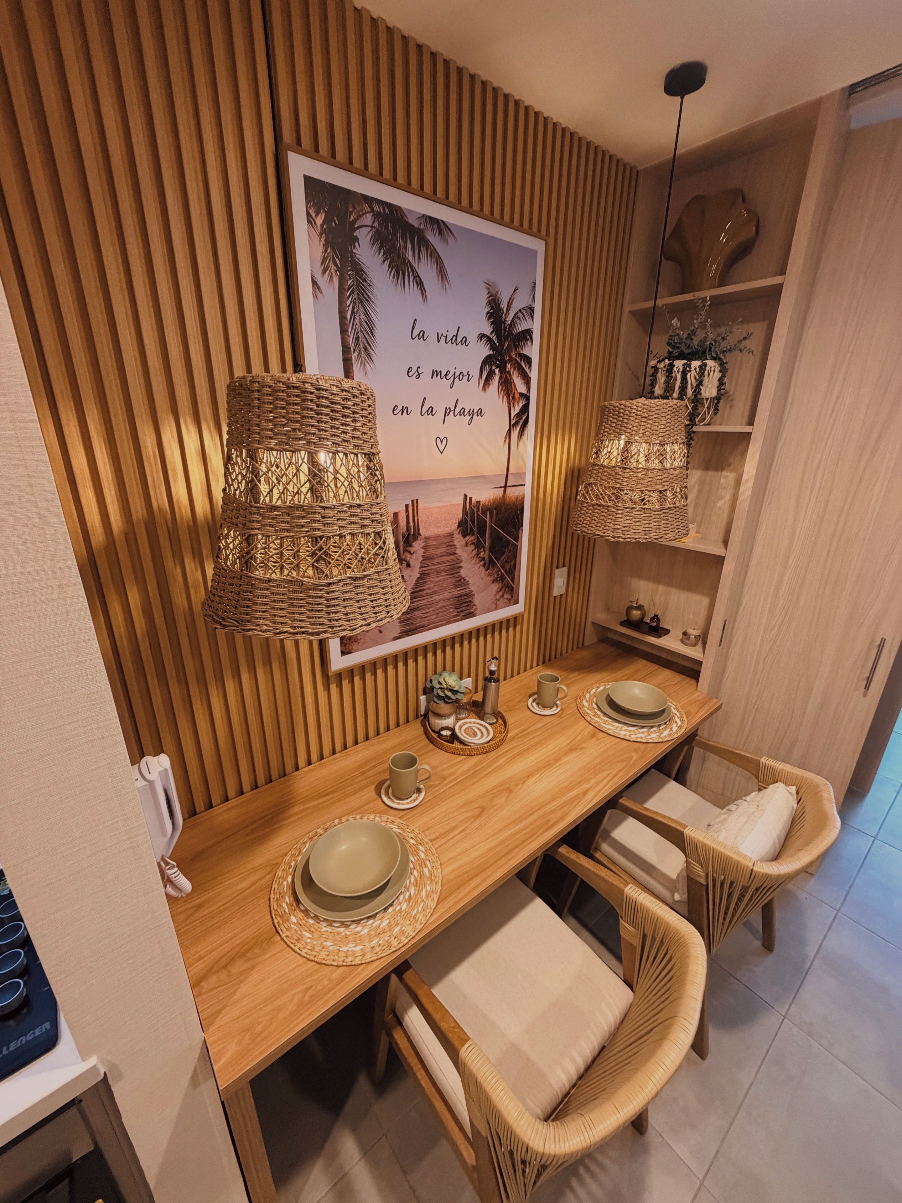 A dining area with a wooden table, wicker lamps, and a framed picture of a beach.