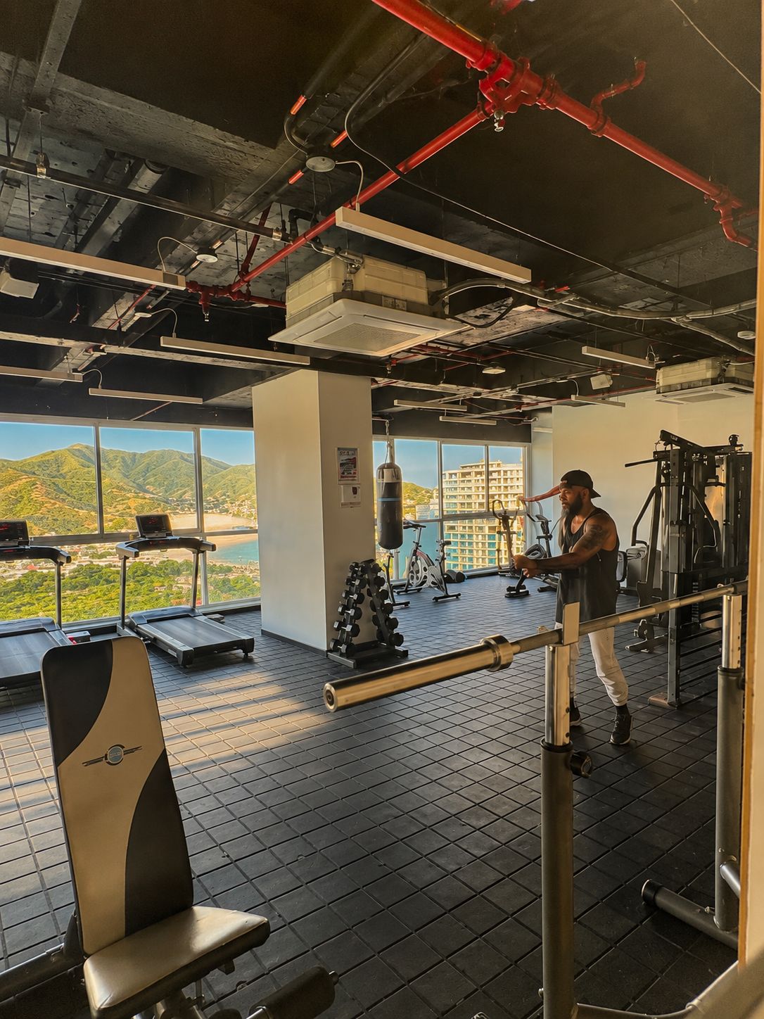 Une salle de sport équipée de matériel d’exercice, d’un sac de frappe et offrant une vue sur les montagnes grâce à de grandes fenêtres.