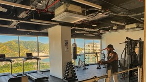Een sportschool met trainingsapparatuur, een bokszak en uitzicht op bergen door grote ramen.