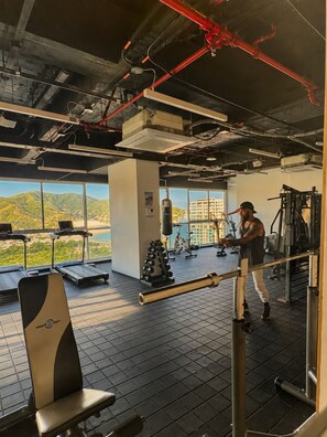 Ein Fitnessstudio mit Trainingsgeräten, einem Sandsack und Blick auf Berge durch große Fenster.