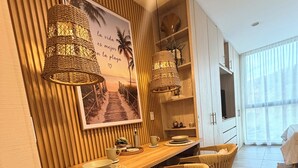 Een eetgedeelte met een houten tafel, rieten lampen en een wanddecoratie met een strandthema.