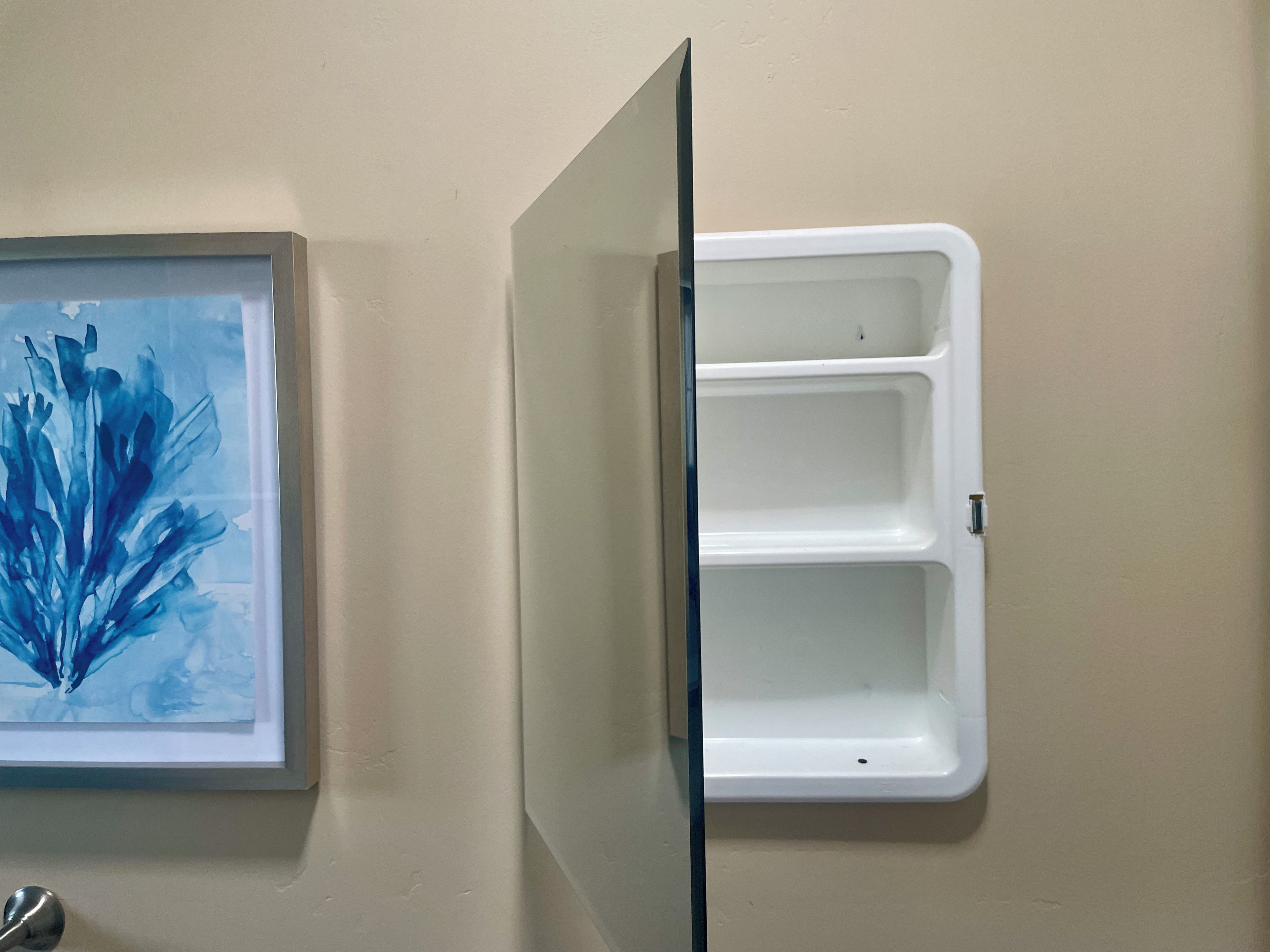 Une salle de bain avec un tableau abstrait encadré au mur et un meuble à pharmacie blanc.