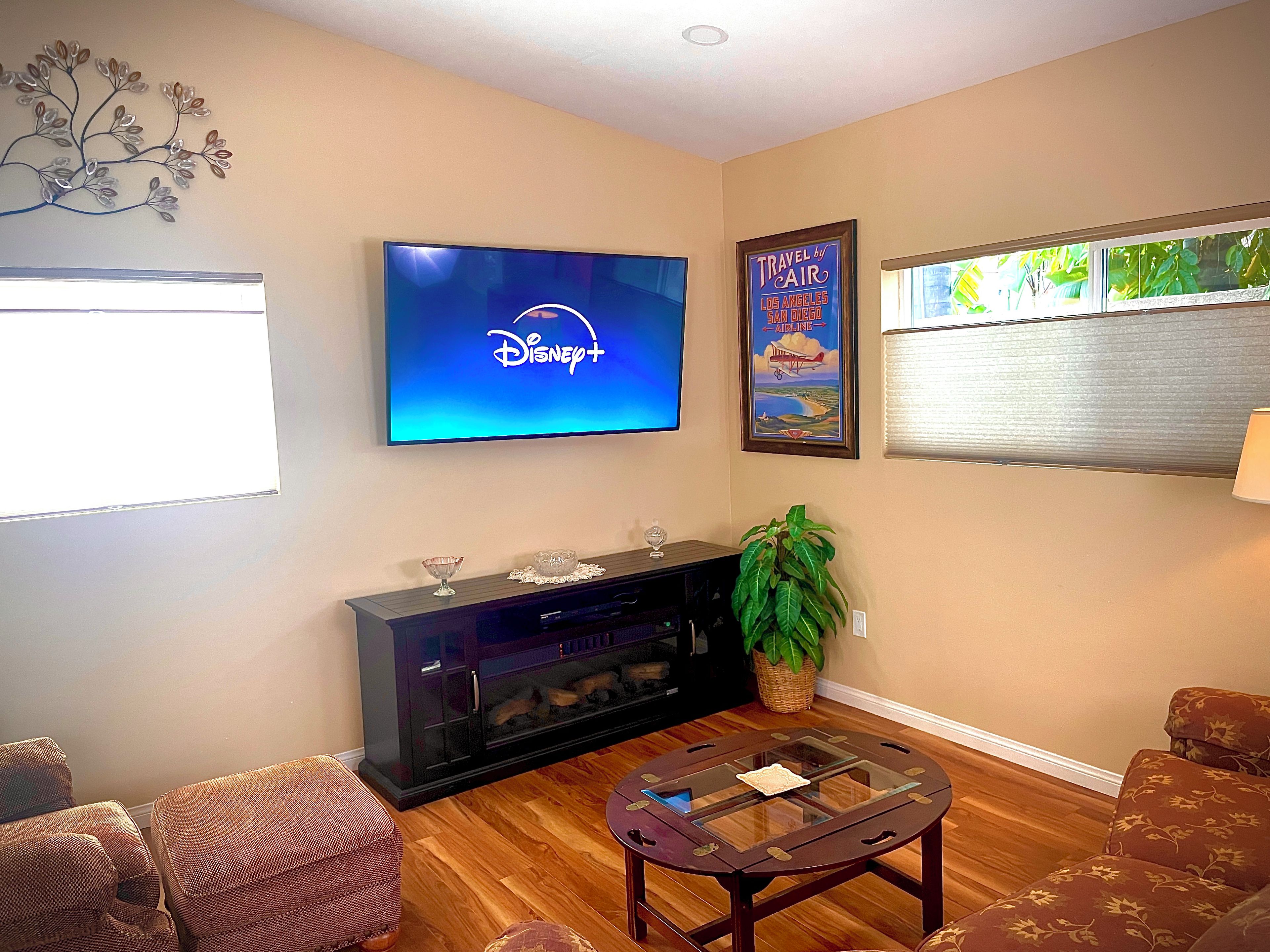 Un salon avec un téléviseur à écran plat affichant le logo de Disney+, une affiche de voyage encadrée, une table basse en verre et une cheminée.