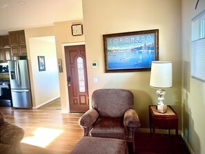A living room with a patterned armchair, a framed picture of Coronado, a clock, and a lamp on a side table. - Lakeside Escape: King Bed, 2 Lakes, 2 Reservoirs, & 30 min.to Beach / San Diego (Lakeside)