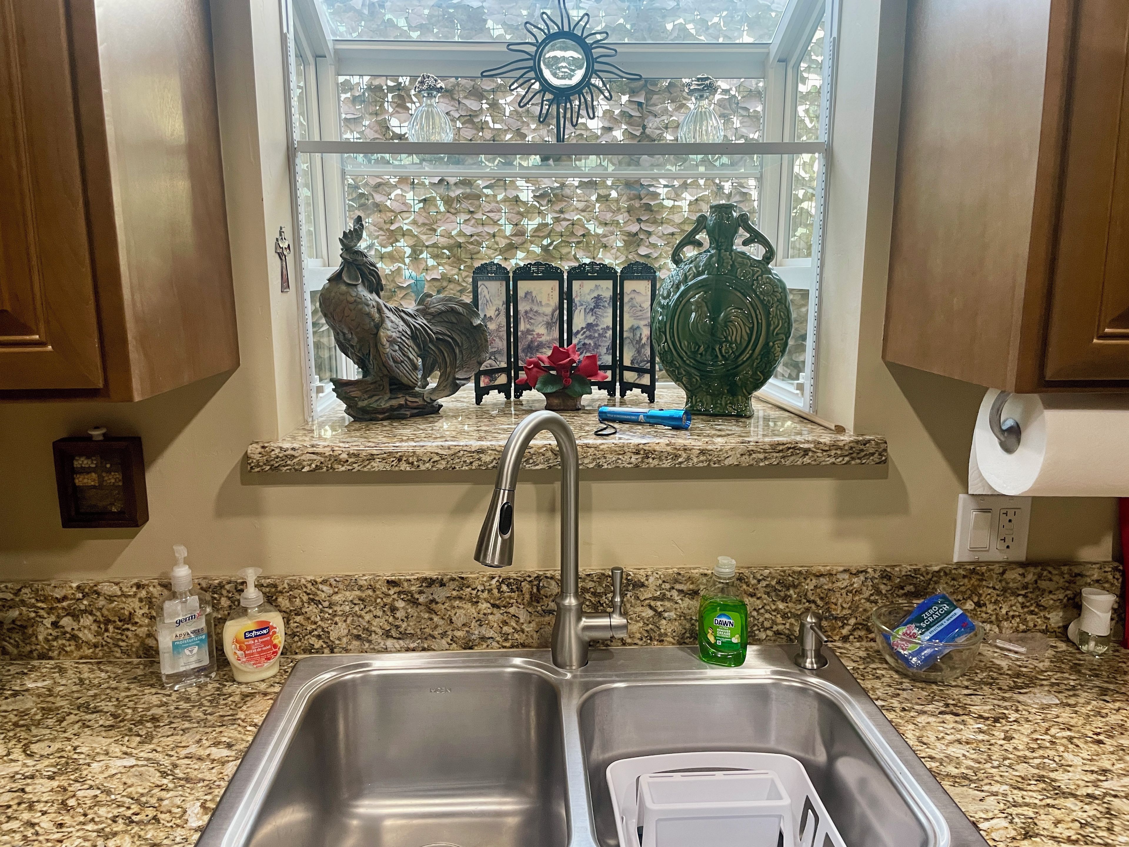 A kitchen with a double sink, granite countertop, and a window with decorative items.