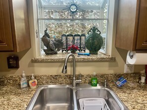 Una cocina con un lavamanos doble, encimera de granito y una ventana decorada con objetos.