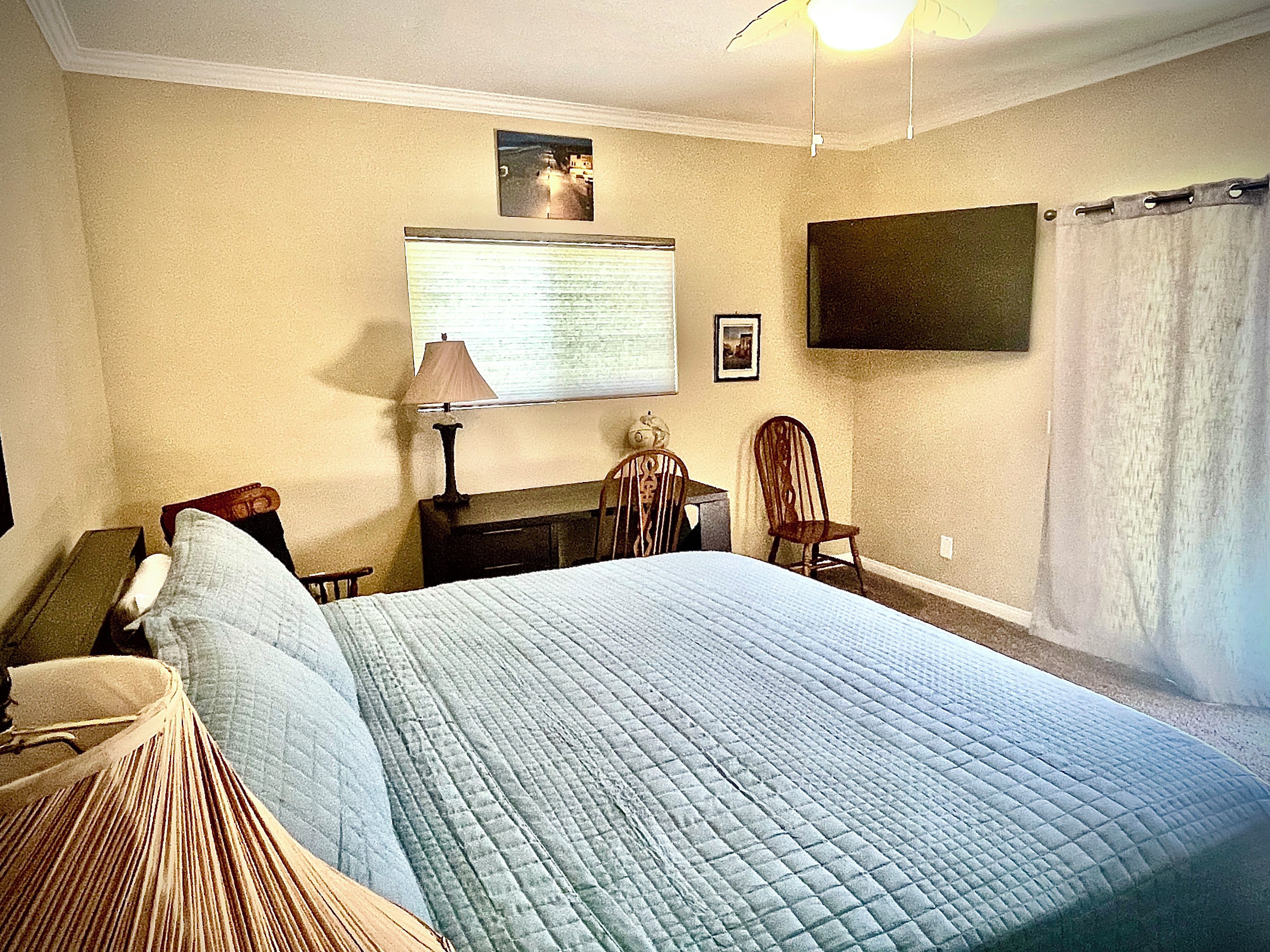 Een slaapkamer met een bed, een bureau, een stoel, een lamp en een televisie aan de muur.